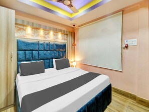 A bedroom with a large bed, a headboard with a textured design, a ceiling fan, and a wall-mounted light fixture. - Collection O Gorchuk Guwahati (Guwahati)