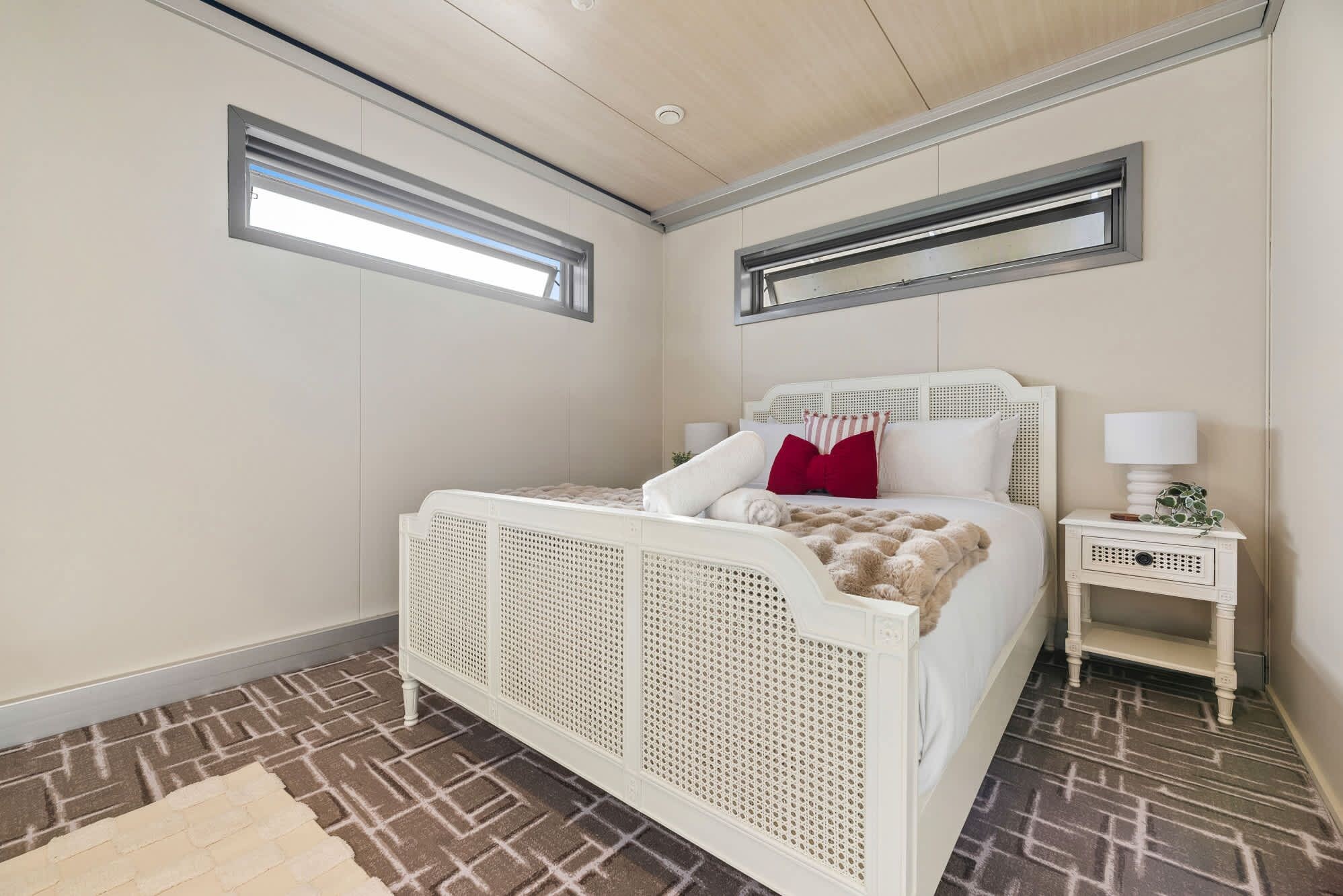 A bedroom with a white bed, a nightstand, a window, and a patterned floor.