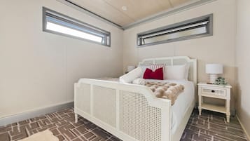 A bedroom with a white bed, a nightstand, a window, and a patterned floor.