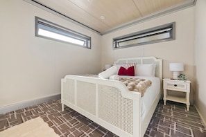 A bedroom with a white bed, a nightstand, a window, and a patterned floor.