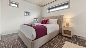 Una camera d'albergo con un letto, un comodino, una lampada e una piccola finestra.