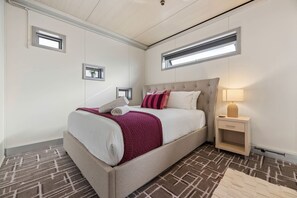A hotel room with a bed, bedside table, lamp, and a small window.