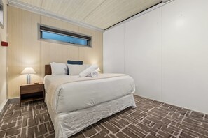 A hotel room with a bed, a nightstand, a lamp, a window, and a patterned carpet.