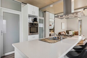 A modern kitchen with a central island, built-in oven, and a dining area with a sofa and chairs. - 2BR Unit For 5, Kangaroo Flat (Kangaroo Flat)