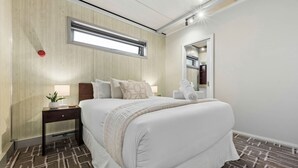Ein Hotelzimmer mit Bett, Nachttisch, Lampe und einem Fenster mit Jalousien.