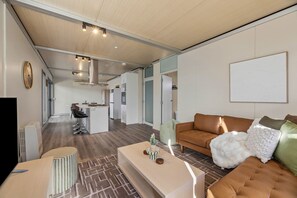 A modern living room with a sofa, a coffee table, and a TV. There is a kitchen area with a dining table and chairs.