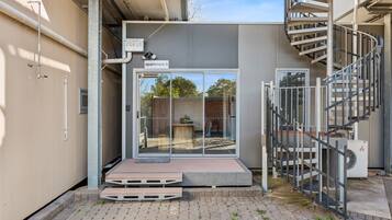 A modern apartment with a glass door entrance, a small outdoor seating area, and a spiral staircase.