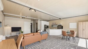 Ein modernes Wohnzimmer mit einer Couch, einem Essbereich mit Stühlen, einer Küche inklusive Geräte und einem Flachbildfernseher.