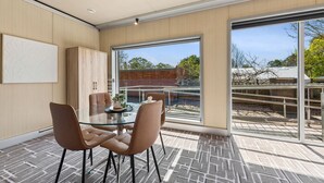 Ein modernes Zimmer mit einem Glastisch, vier Stühlen, einem Schrank und einem großen Fenster mit Blick ins Freie.