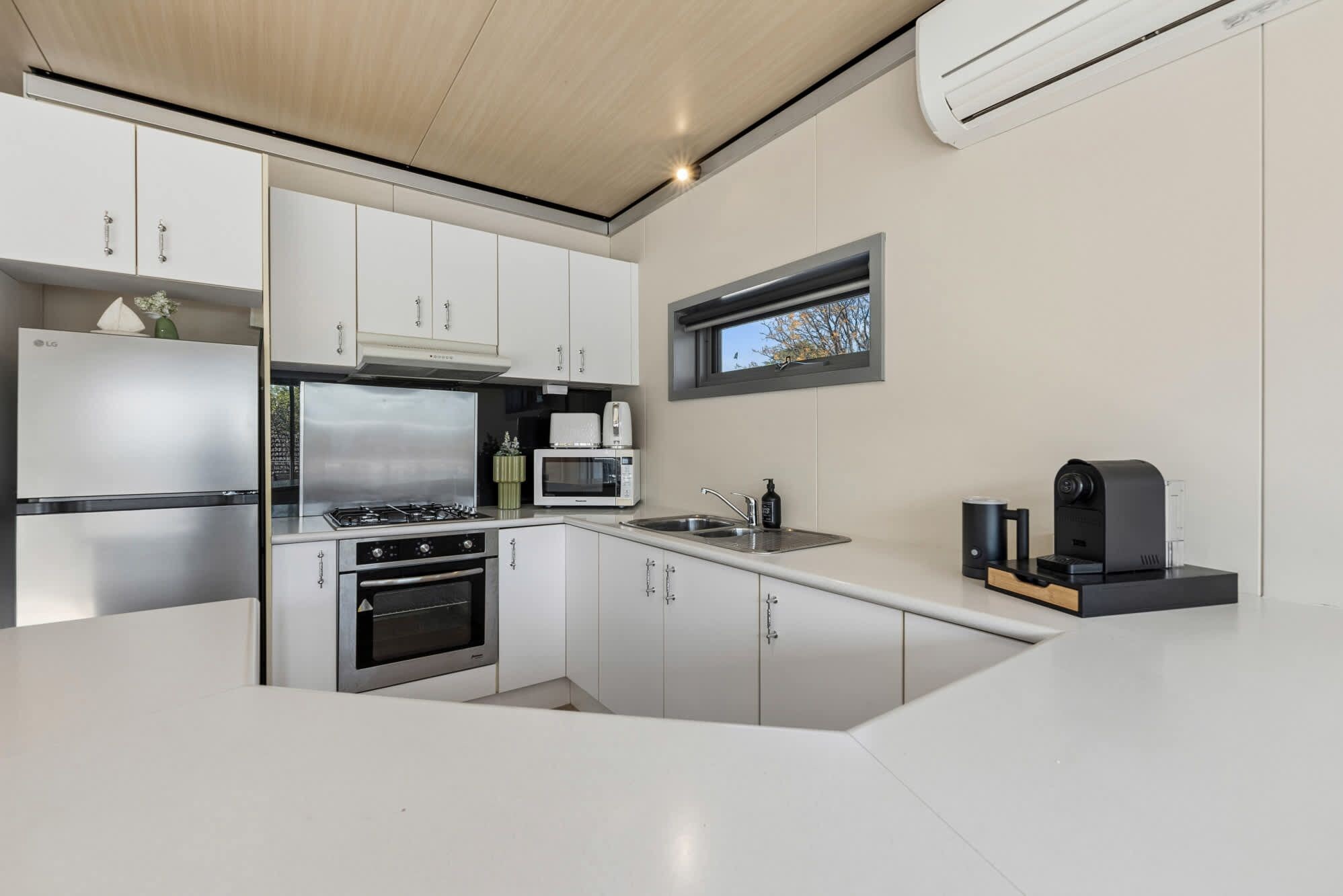 A compact kitchen with white cabinets, a stainless steel stove, a microwave, and a coffee machine.