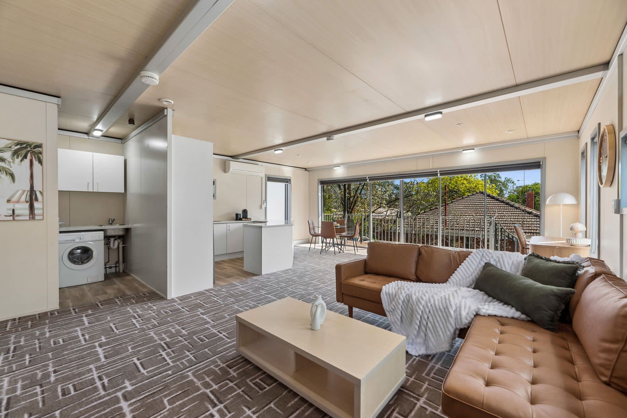 A modern living room with a sofa, coffee table, and a view of the kitchen and outdoor area.