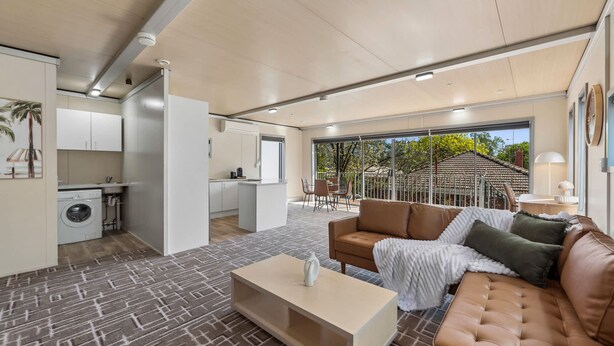 A modern living room with a sofa, coffee table, and a view of the kitchen and outdoor area. - Cosy 2BR Kangaroo Flat Unit (Kangaroo Flat)
