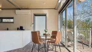 A modern outdoor dining area with a glass table and chairs, a small kitchen area with a sink and coffee maker, and a view of the outdoors through large windows. - Cosy 2BR Kangaroo Flat Unit (Kangaroo Flat)