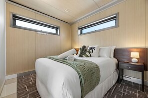 Ein Hotelzimmer mit einem Bett, Nachttischen, einer Lampe und zwei Fenstern.