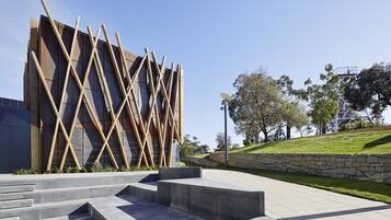 A modern building with a unique geometric facade, a landscaped area with steps, and a clear sky.
