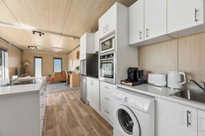 Una cuina moderna amb armaris blancs, forn de sobre, microones, cafetera i rentadora.