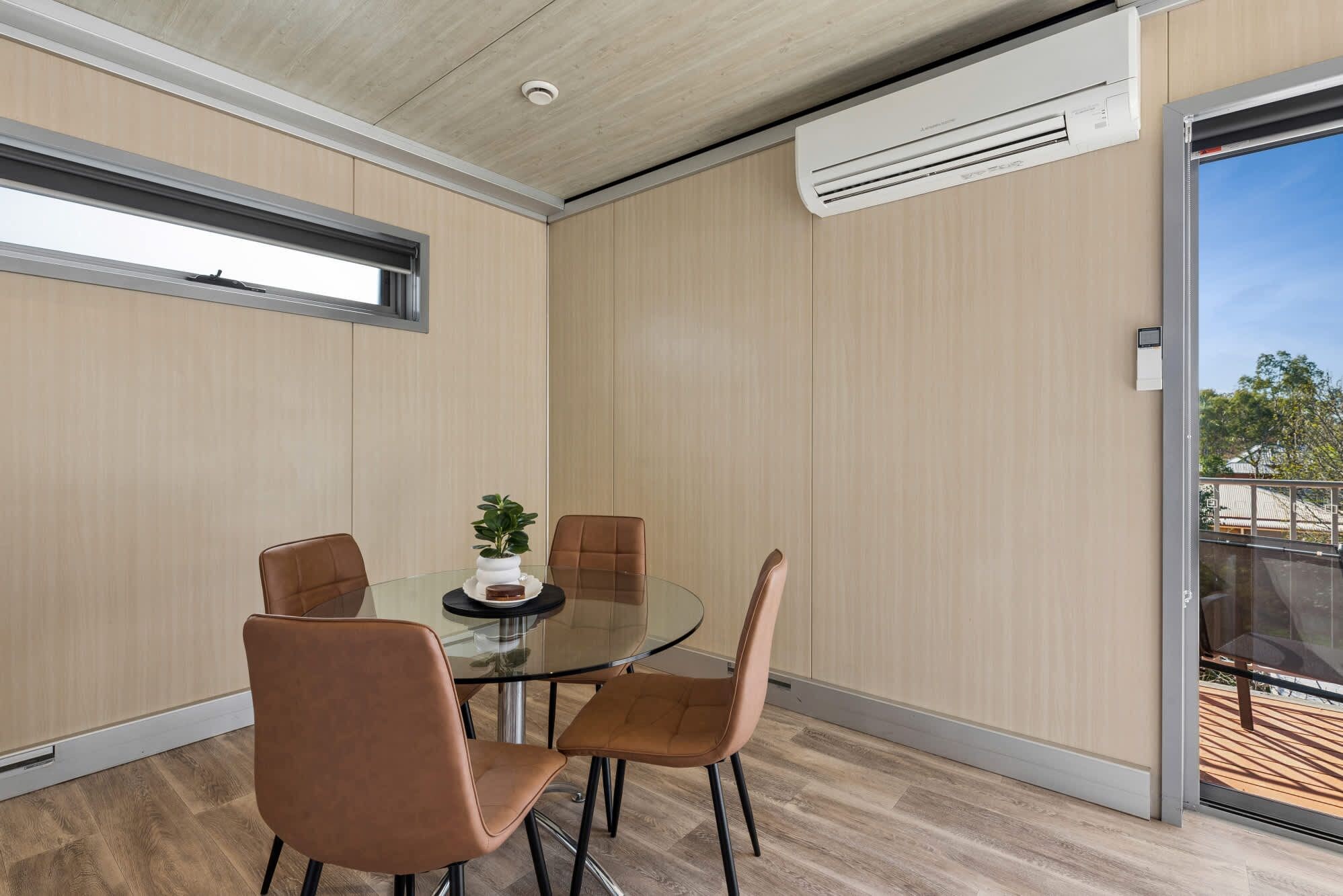 A modern room with a glass table, four chairs, a potted plant, and an air conditioning unit.