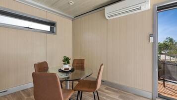 A modern room with a glass table, four chairs, a potted plant, and an air conditioning unit.