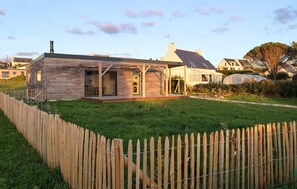 Ein Holzhaus mit eingezäuntem Garten, einer überdachten Terrasse und einem Gewächshaus.