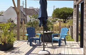 Eine Holzterrasse mit zwei blauen Stühlen und einem Tisch, umgeben von Pflanzen und einem Zaun.