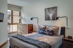 A bedroom with a bed, bedside lamps, a dresser, a window, and a wall-mounted artwork. - Cozy 1BR Mountain Village Palmyra Condo with Fireplace and Ski Views (Telluride)