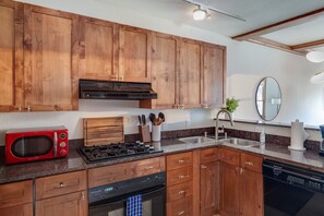 A modern kitchen with wooden cabinets, a red microwave, a gas stove, and a built-in oven. - Cozy 1BR Mountain Village Palmyra Condo with Fireplace and Ski Views (Telluride)