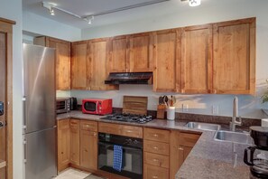 A modern kitchen with wooden cabinets, stainless steel appliances, a red microwave, and a gas stove. - Cozy 1BR Mountain Village Palmyra Condo with Fireplace and Ski Views (Telluride)