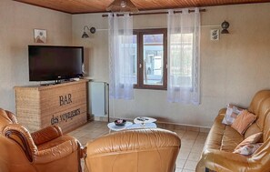 A living room with a television on a wooden cabinet, leather sofas, a small table, and a window with curtains. - Gite nature sur Priziac (Priziac)