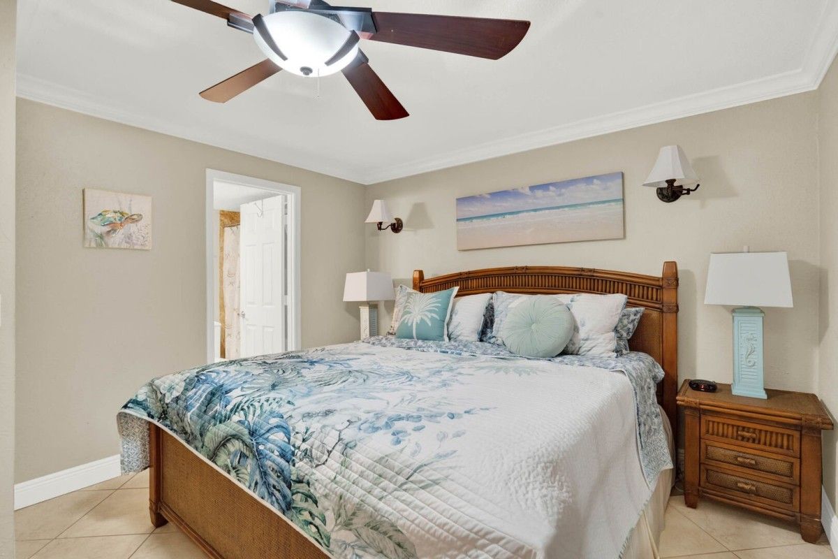 A bedroom with a wooden bed, a ceiling fan, a nightstand with a lamp, and a painting on the wall.