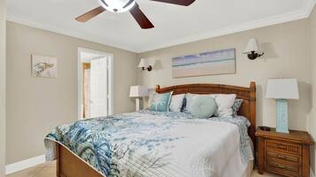 A bedroom with a wooden bed, a ceiling fan, a nightstand with a lamp, and a painting on the wall.