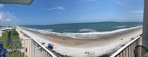 A beach view from a balcony with a railing, a flag, and beach umbrellas.