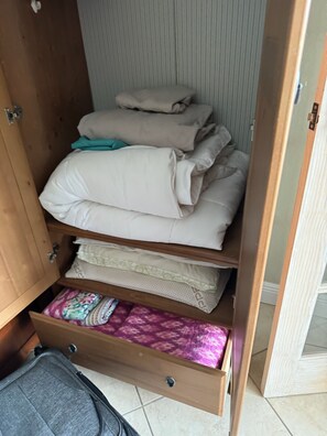 Ein Holzkleiderkasten mit mehreren Einlegeböden, auf einigen liegen gefaltete Bettwäsche, andere sind mit Schubladen ausgestattet.