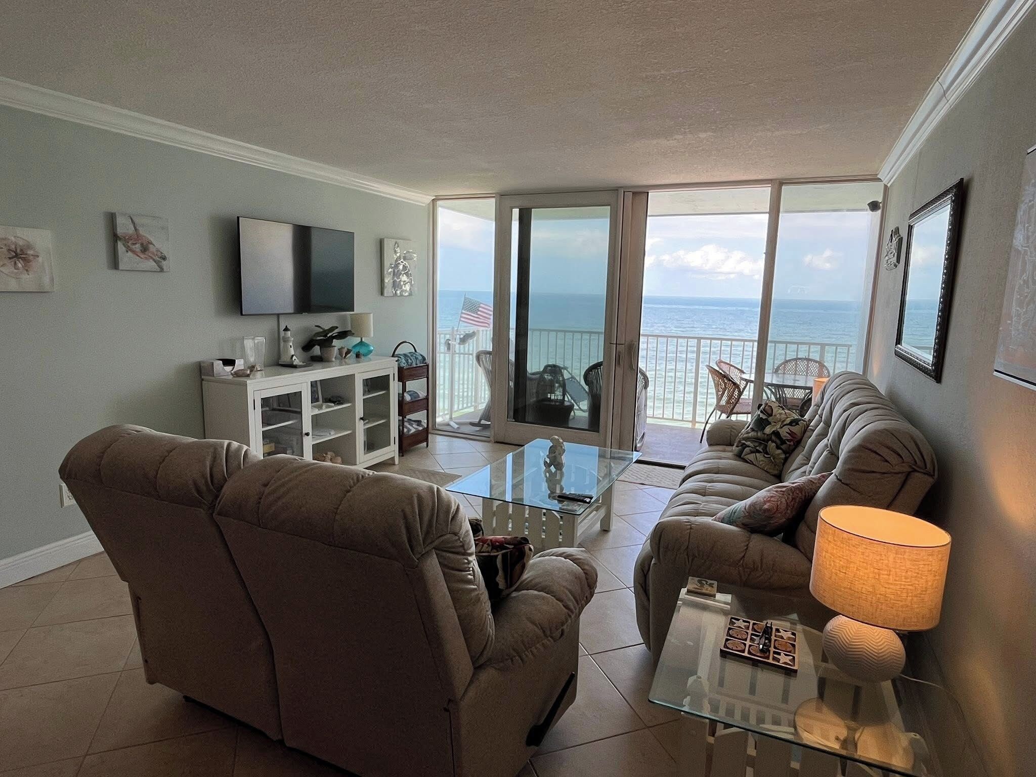 A living room with a sofa, armchair, TV, and a glass coffee table.