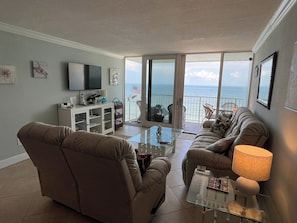 A living room with a sofa, armchair, TV, and a glass coffee table.