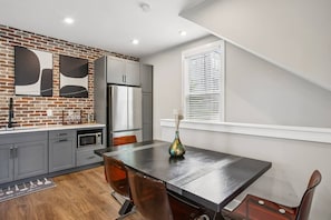 A modern kitchen with a brick accent wall, stainless steel appliances, and a dining area with a table and chairs. - Prime Location, Walk to Food and Drinks, Close to Downtown Atl (Atlanta)