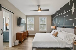 A bedroom with a bed, a TV, a ceiling fan, and a wall with geometric patterns. - Prime Location, Walk to Food and Drinks, Close to Downtown Atl (Atlanta)