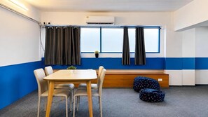 Una habitación con una mesa, sillas, un banco y una ventana con cortinas.