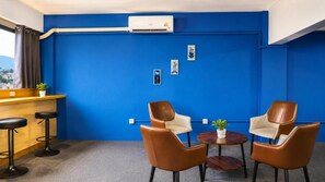 Una habitación con pared azul, una zona con barra de madera, dos sillones de cuero, una mesita y un equipo de aire acondicionado.