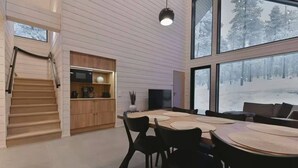 A modern interior with a dining area, kitchen, and large windows offering a view of a snowy landscape. - Villa QUU C,  Premium 4BD Villa with Sauna (Kolari)