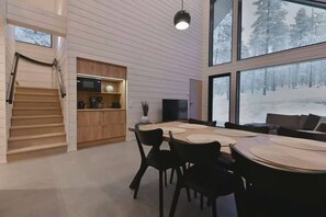 A modern interior with a dining area, kitchen, and large windows offering a view of a snowy landscape. - Villa QUU C,  Premium 4BD Villa with Sauna (Kolari)