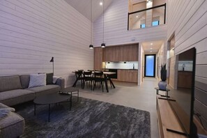 A modern interior with a sofa, dining table, and chairs, a kitchen area, and a staircase leading to an upper level.