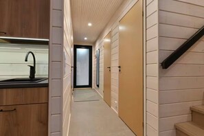 A narrow hallway with a kitchen area on the left, featuring a sink and cabinets. There are doors on the right side, leading to a staircase.