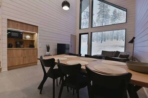 A modern interior with a dining area, kitchen, and large windows offering a snowy forest view.