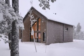 Een houten chalet met een groot raam en een deur, omgeven door met sneeuw bedekte bomen.
