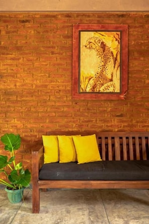 A wooden bench with yellow cushions against a brick wall, a framed picture of a cheetah, and a potted plant.