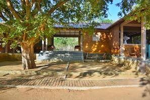 A covered outdoor area with a brick building, a large tree, and a paved walkway.