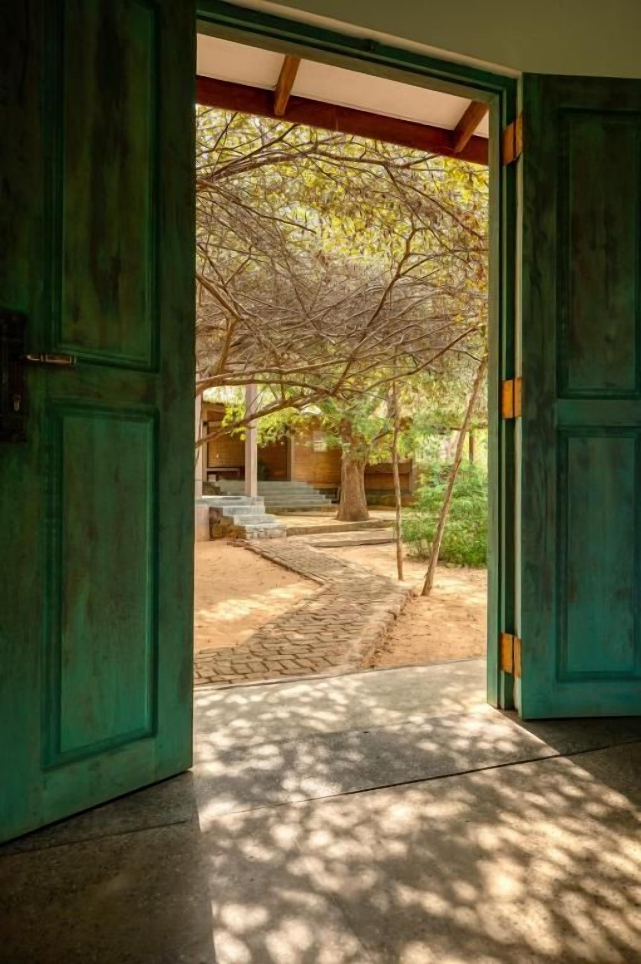 Puerta abierta que da a un espacio exterior cubierto, con un sendero de piedra y un banco.