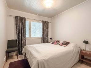 A bedroom with a bed, curtains, a chair, a nightstand, and a window. - Ruka nature: sauna, WiFi, cleaning incl. (Kuusamo)