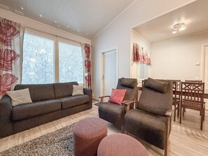 Ein Wohnzimmer mit einer Couch, Sesseln, einem Hocker und einem Essbereich mit Stühlen und einem Tisch.