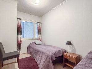 Ein Schlafzimmer mit einem Bett, einem Sessel, einem Nachttisch und einem Fenster mit Vorhängen.